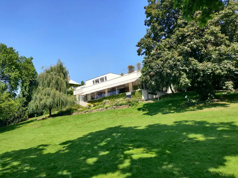 Maison basse posée dans une pente herbeuse plantée de vieux arbres
